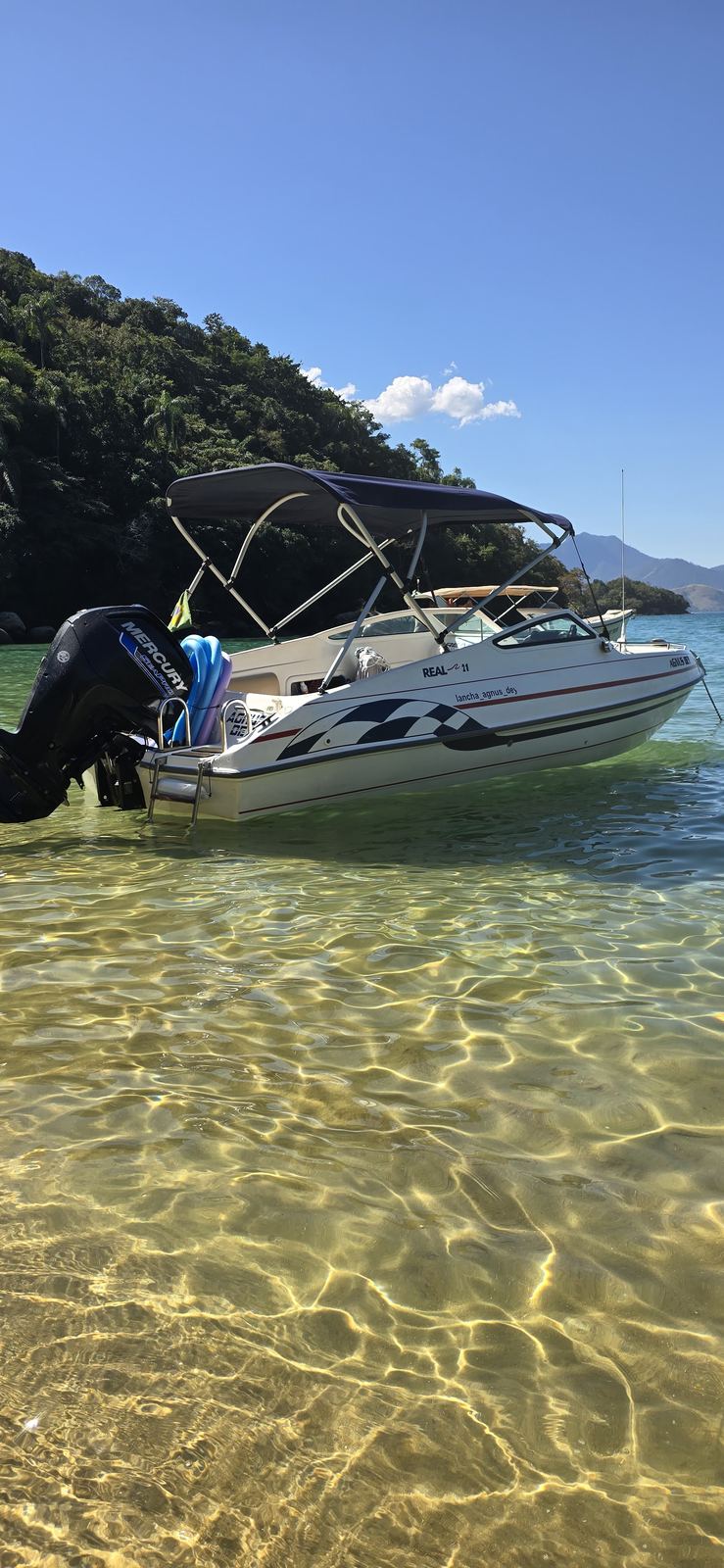 Lancha parada em água rasa e transparente junto à faixa de areia